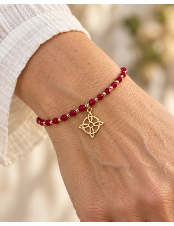 Pulsera roja ajustable con dije circular de cuatro puntas bañada en oro puesta en la muñeca