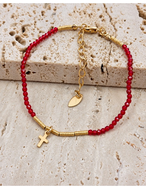 Pulsera roja con cruz y tubos texturados bañada en oro sobre piedra beige
