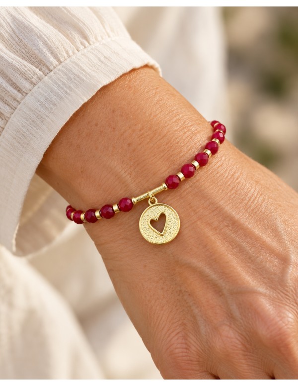 Pulsera roja con medalla de corazón calado bañada en oro puesta en la muñeca