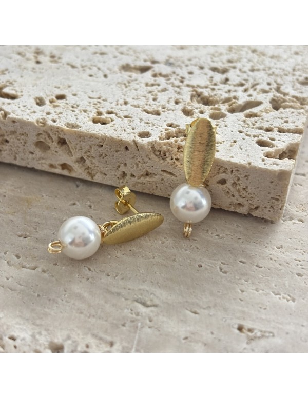 Detalle de aros ovalados texturizados bañados en oro con perlas shell blancas de 8 mm sobre piedra
