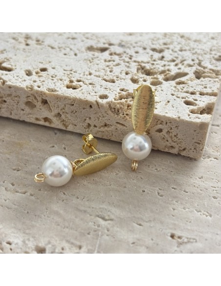 Detalle de aros ovalados texturizados bañados en oro con perlas shell blancas de 8 mm sobre piedra