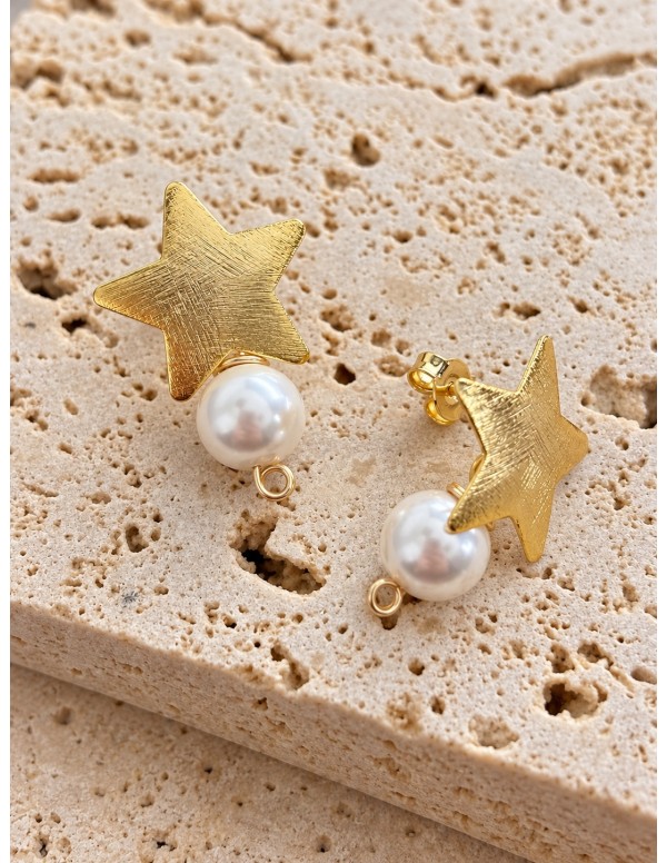 Detalle de aros estrella bañados en oro con perlas shell blancas de 8 mm sobre piedra beige