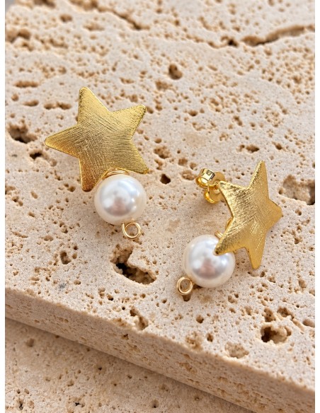 Detalle de aros estrella bañados en oro con perlas shell blancas de 8 mm sobre piedra beige