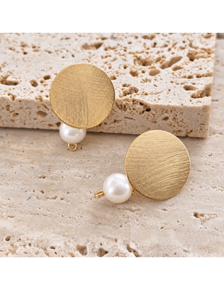 Detalle de aros circulares bañados en oro con textura lijada y perlas blancas sobre piedra beige